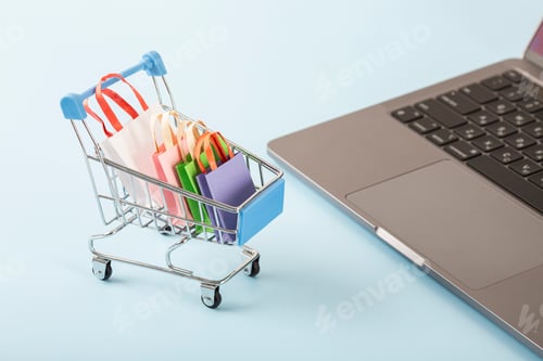 Preview: Online shopping concept. Shopping cart, small boxes, laptop on the desk