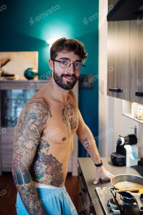 Preview: Mid adult man with tattooed chest preparing breakfast, portrait
