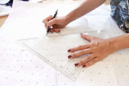 Preview: Hands diligently plotting a pattern on dotted paper with rulers and pen.