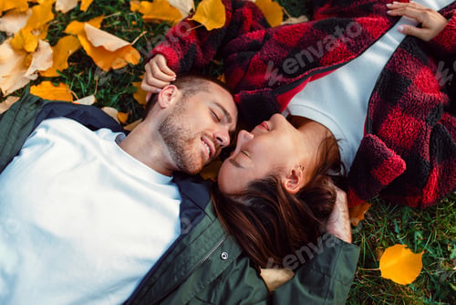 Preview: Multicultural couple lying on autumn leaves smiling and cuddling outdoors.