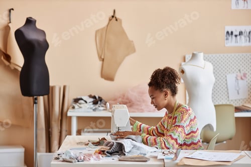 Preview: Long shot of young female artisan upcycling old clothes in workshop