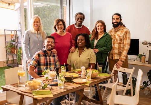 Preview: Group of friends gathering around table with food and drinks smiling at camera