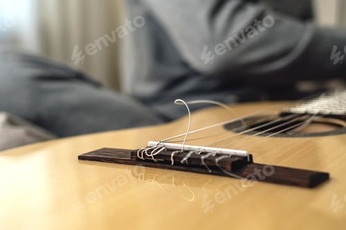 Preview: Sitting on the bed, the guy pulls a broken string on an acoustic guitar