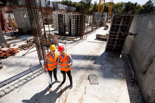 Preview: Civil engineer and architect dressed in orange work vests and hard bats discuss the construction