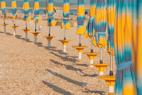Preview: Folded colorful beach umbrella parasols on Adriatic sea coast in sunny summer morning