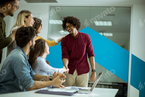Preview: Group of young coworkers interacting around a table and handshaking in the office