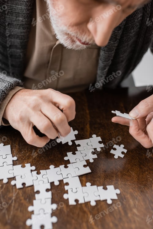 Preview: cropped view of senior man with parkinson disease and tremor in hands combining jigsaw puzzle on