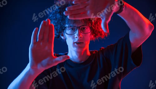Preview: Gesture of making photo. Young man with curly hair is indoors illuminated by neon lighting
