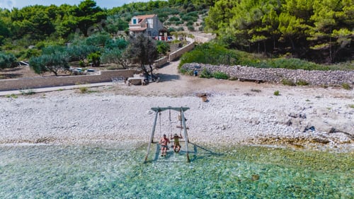 Preview: Joyful children playing on a swing by the crystal-clear waters of Brac Island, Croatia in summer