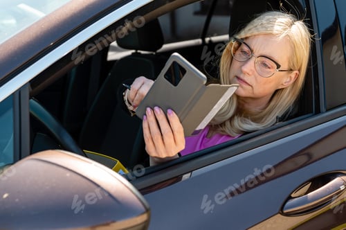 Preview: a middle aged blonde woman in glasses with a smartphone looks through an open car window