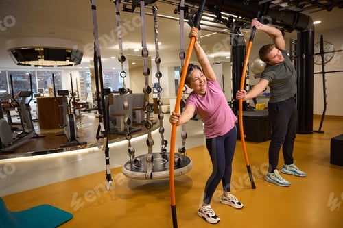 Preview: Male trainer and middle aged smiling woman doing exercise with sports sticks