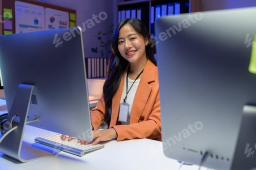 Preview: Young Asian businesswoman working late at night in office typing on computer keyboard and smiling
