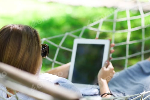 Preview: Man in hat in a hammock with tablet computer on a summer day