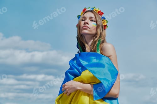 Preview: Confident Ukrainian woman in floral crown covering with national flag with sky in the background