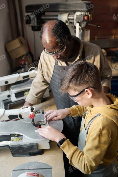 Preview: Boy Cutting Wood Using Machine Tools in Workshop with Master Helping