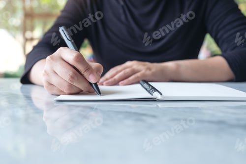 Preview: Closeup image of business woman writing on blank notebook on table with green nature background