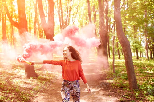 Preview: Happy girl laughing and running with pink color smoke bomb in forest.