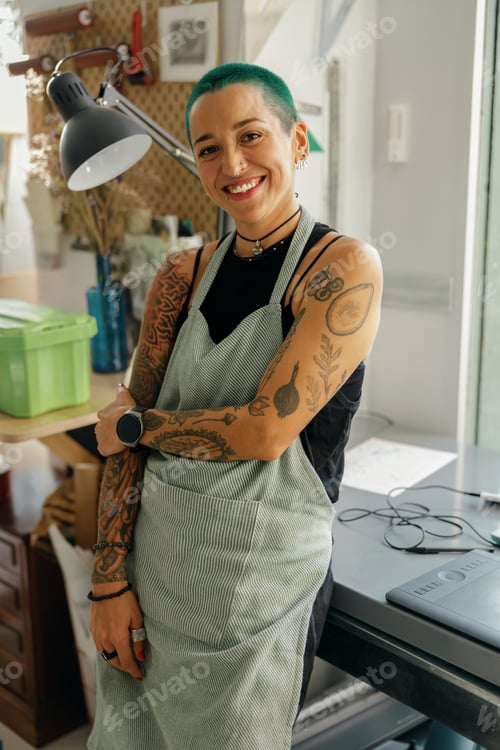 Preview: Creative female worker sitting on background of own design studio and looks camera with smile