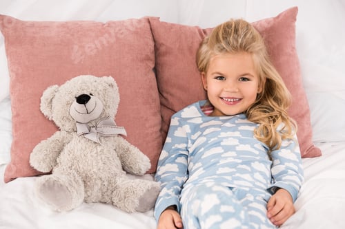 Preview: adorable smiling child lying in bed with teddy bear
