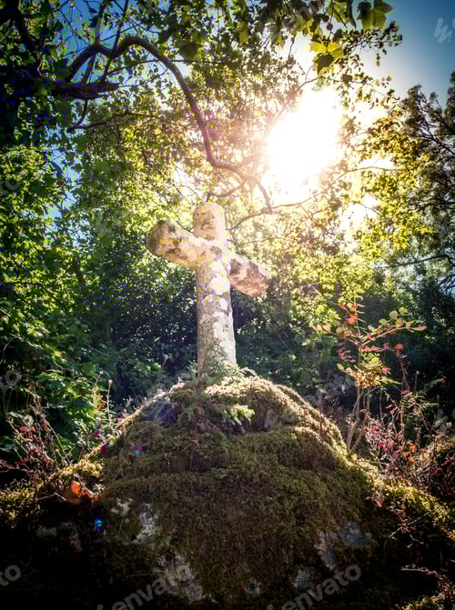Preview: Low angle shot of an old stone cross on top of a hill covered with moss