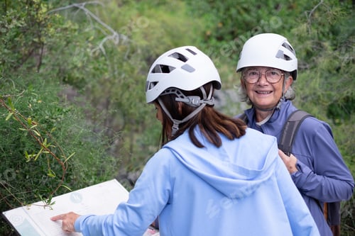 Preview: Smiling couple of senior hiker women in protective helmets checking map directions in mountain hike