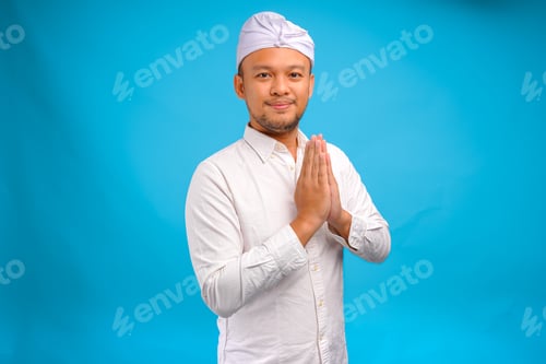 Preview: Handsome young Balinese man wearing Indonesian traditional udeng doing greeting or welcome gesture.