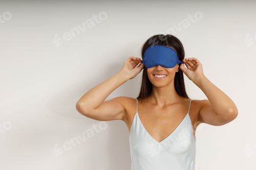 Preview: Healthy young woman dressing nightie put on sleep mask sitting on bed in bedroom