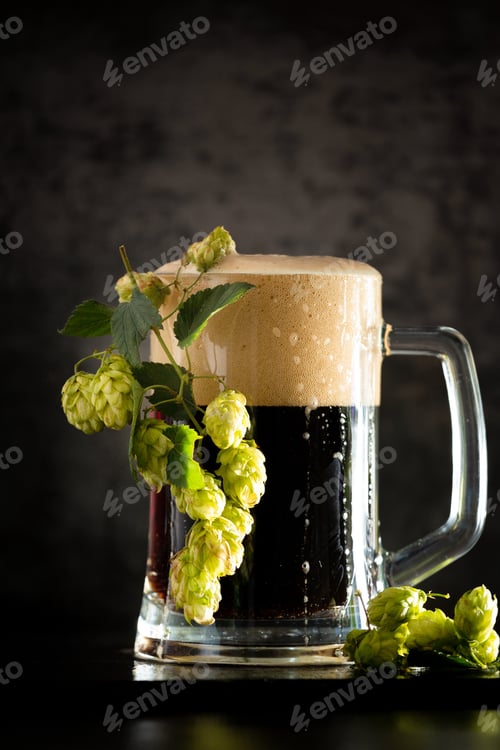 Preview: Glass of dark beer with hops around on a dark background
