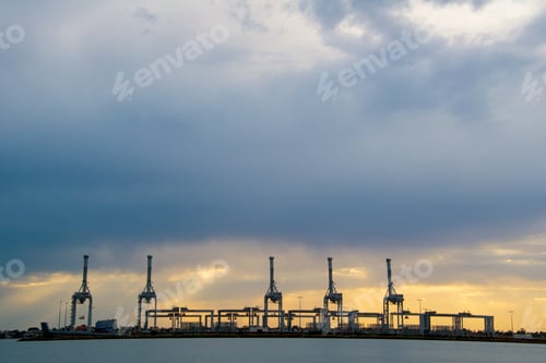 Preview: Industrial port cranes silhouetted against a dramatic, cloud-filled sky at sunset