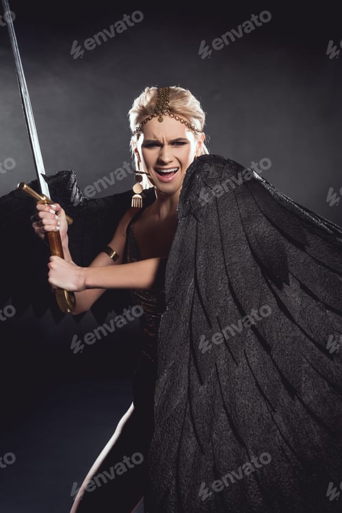 Preview: beautiful angry woman in warrior costume with angel wings holding sword and posing on black
