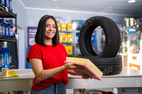 Preview: Woman holding an air filter, standing in an auto parts store with tires on display