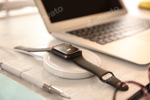 Preview: Smartwatch with wireless charger on white wooden table. Modern workplace accessory