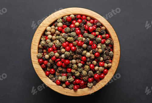 Preview: Aromatic peppercorns in bowl on dark table, top view