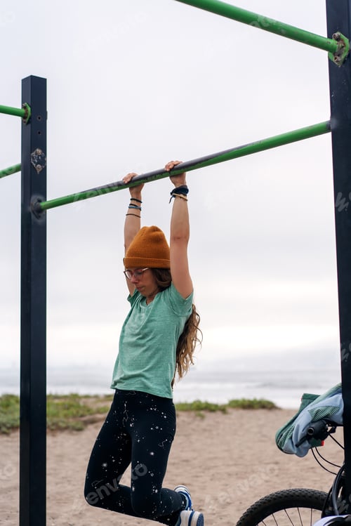Preview: young woman workout on pull up bar outdoors on the beach