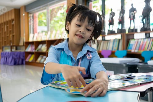 Preview: A schoolgirl wearing a hearing aid sits in the school library reading a book.