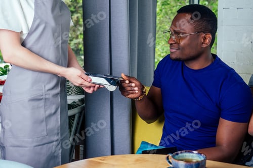 Preview: mixed-race friends paying to waiter payment machine in cafe