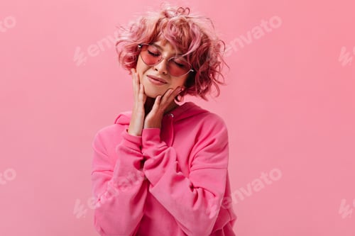 Preview: Cute pretty curly woman in bright hoodie poses on pink background. Charming short-haired girl in su