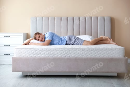 Preview: Young man lying on bed with soft mattress at home