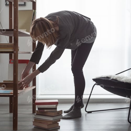 Preview: Woman bending forward to arrange books on living room bookshelf