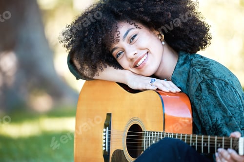 Preview: Smiling young musician resting on her acoustic guitar while playing and enjoying a day in the park.