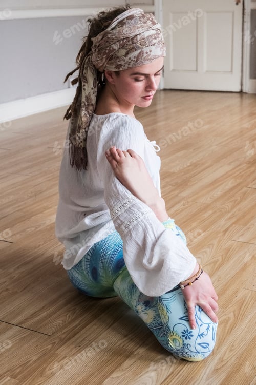 Preview: Young woman wearing headscarf and white blouse sitting on floor in yoga pose.