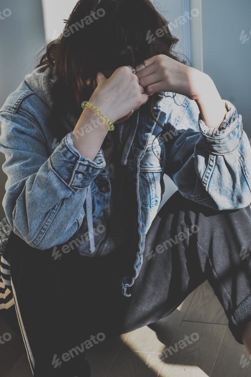 Preview: Upset teenage girl sitting on a floor, covering her face