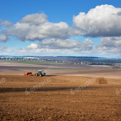 Preview: panoramic view of arable lands, tractor with seeder at sowing time