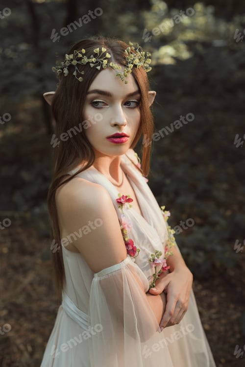 Preview: beautiful female elf in flower dress and wreath standing with crossed arms in forest