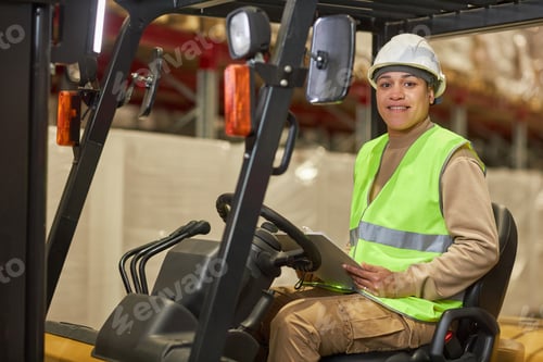 Preview: Smiling black woman operating forklift truck in warehouse