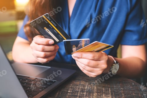 Preview: Closeup image of a woman holding and choosing credit cards while using laptop computer
