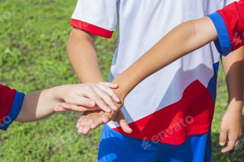 Preview: A close-up of the cut arms of three young footballers. The players' palms are on top of each other.