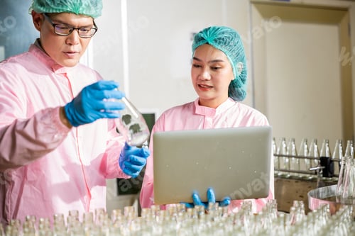 Preview: Two engineers oversee quality control checking product bottles on a beverage factory's conveyor belt