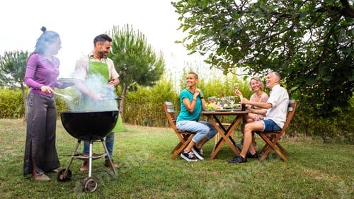 Preview: Multiracial couple cooking food on grill for friends. Outdoor garden barbecue party.