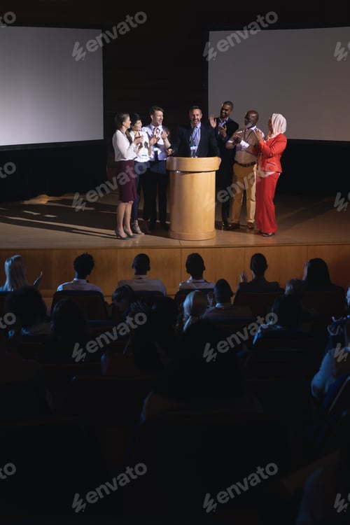 Visualização: Diversos colegas de trabalho batendo palmas para seu colega no palco do auditório